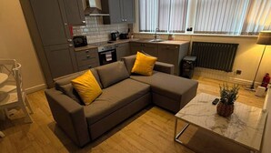 Eine moderne Küche mit grauen Schränken, ein Essbereich mit einem braunen Sofa und gelben Kissen sowie ein kleiner Tisch mit einer Pflanze.