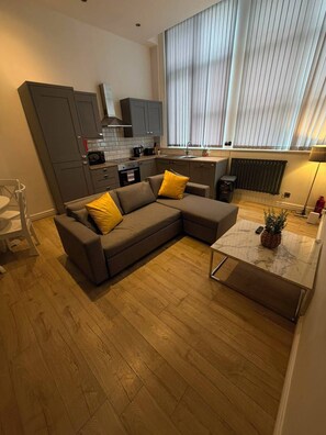 Eine moderne Küche mit grauen Schränken, ein Essbereich mit einem braunen Sofa und gelben Kissen sowie ein kleiner Tisch mit einer Pflanze.