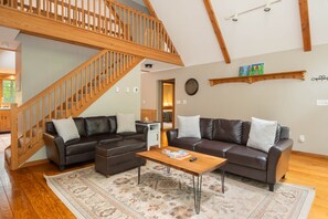 Ein geräumiges Wohnzimmer mit einer Holztreppe, zwei Ledersofas, einem Couchtisch und einem gemusterten Teppich.