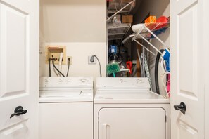 Ein Waschraum mit zwei Waschmaschinen und Trocknern mit Frontlader, einem Warmwasserbereiter und einem Wäschewagen voller Reinigungsmittel.