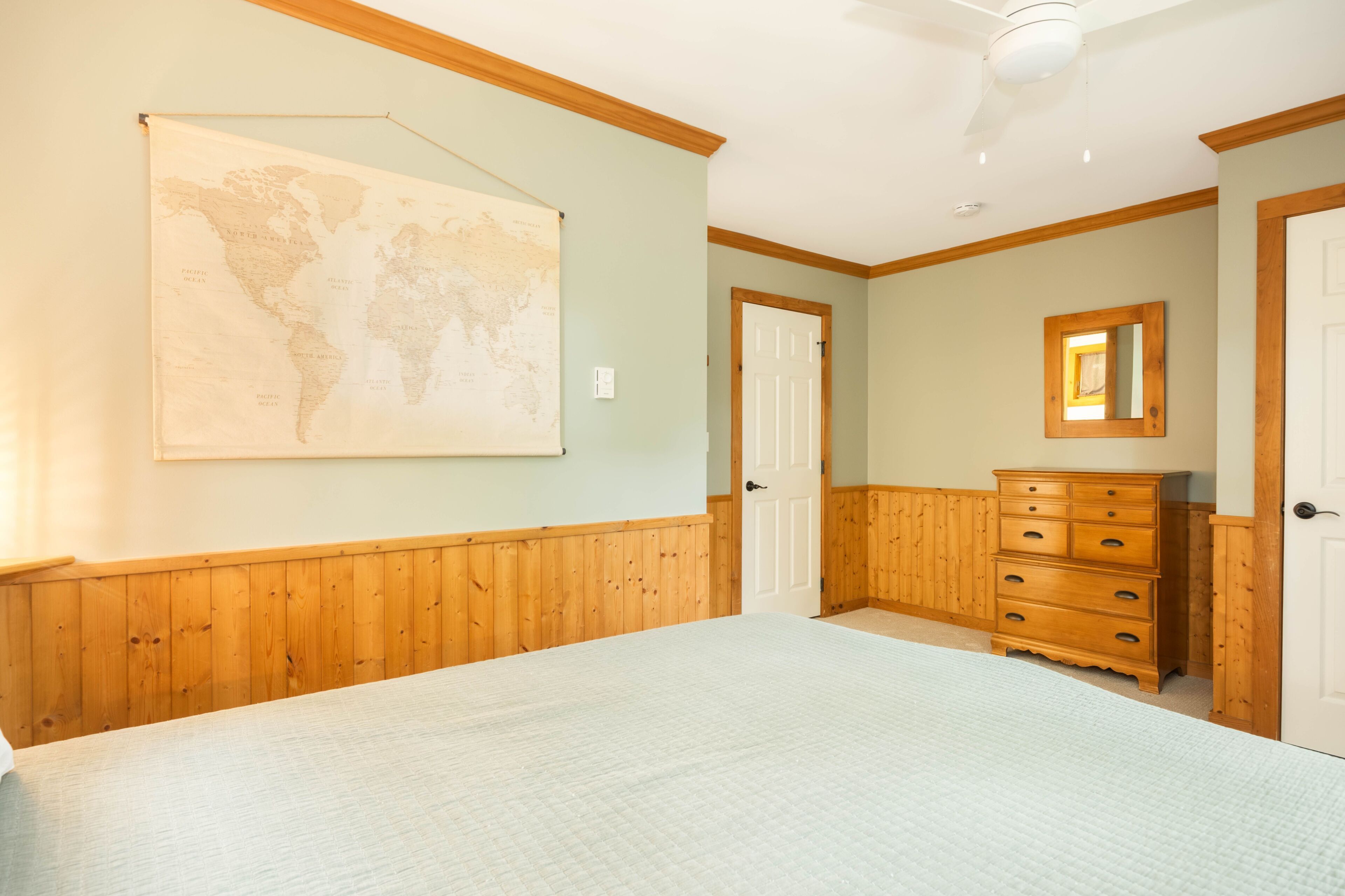 A bedroom with a bed, a dresser, a mirror, and a world map on the wall.