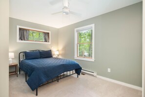 A bedroom with a bed, two bedside lamps, a ceiling fan, and two windows with curtains. - FirePit, Hot Tub, Dock + Lake "Get Your Creek On" (Swanton)