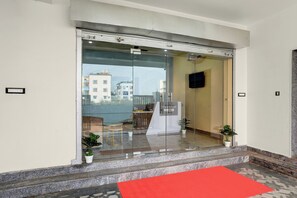 Entrada de un hotel con puerta de cristal, alfombra roja y vista de edificios.