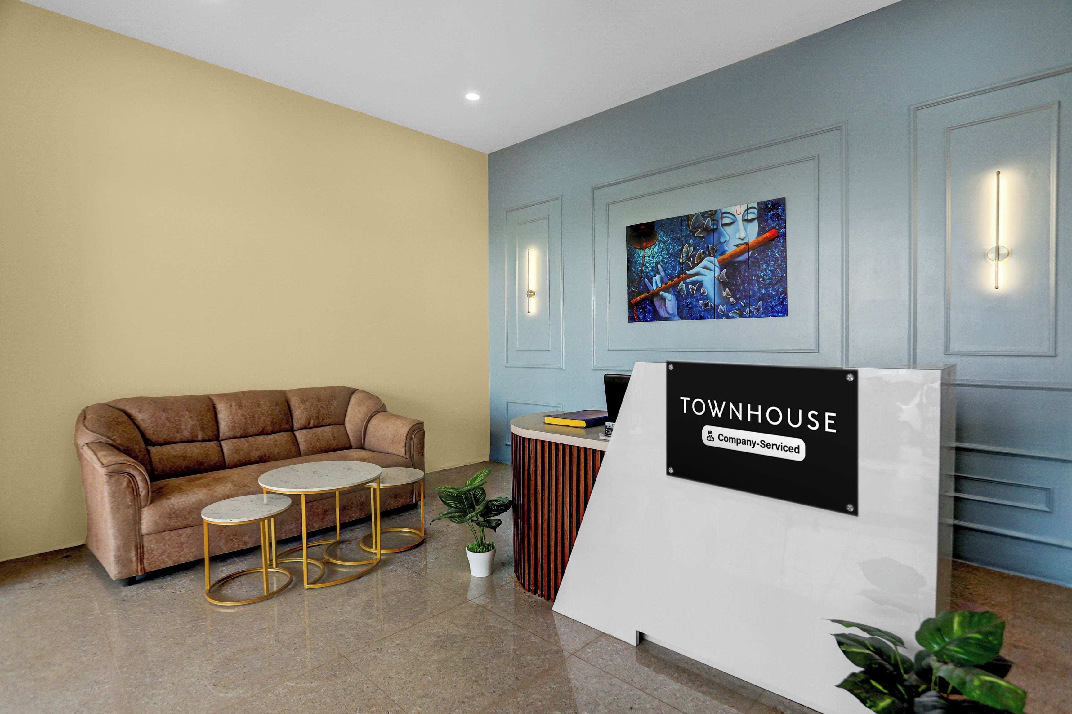 A reception area with a brown sofa, two small round tables, a potted plant, and a sign that reads 'TOWNHOUSE Company-Serviced'.