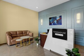 Un área de recepción con un sofá marrón, dos mesitas redondas, una planta en maceta y un letrero que dice 'TOWNHOUSE Company-Serviced'.