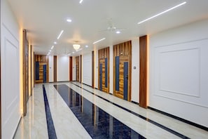 Un largo pasillo con puertas a un lado y un suelo de mármol que refleja la luz.