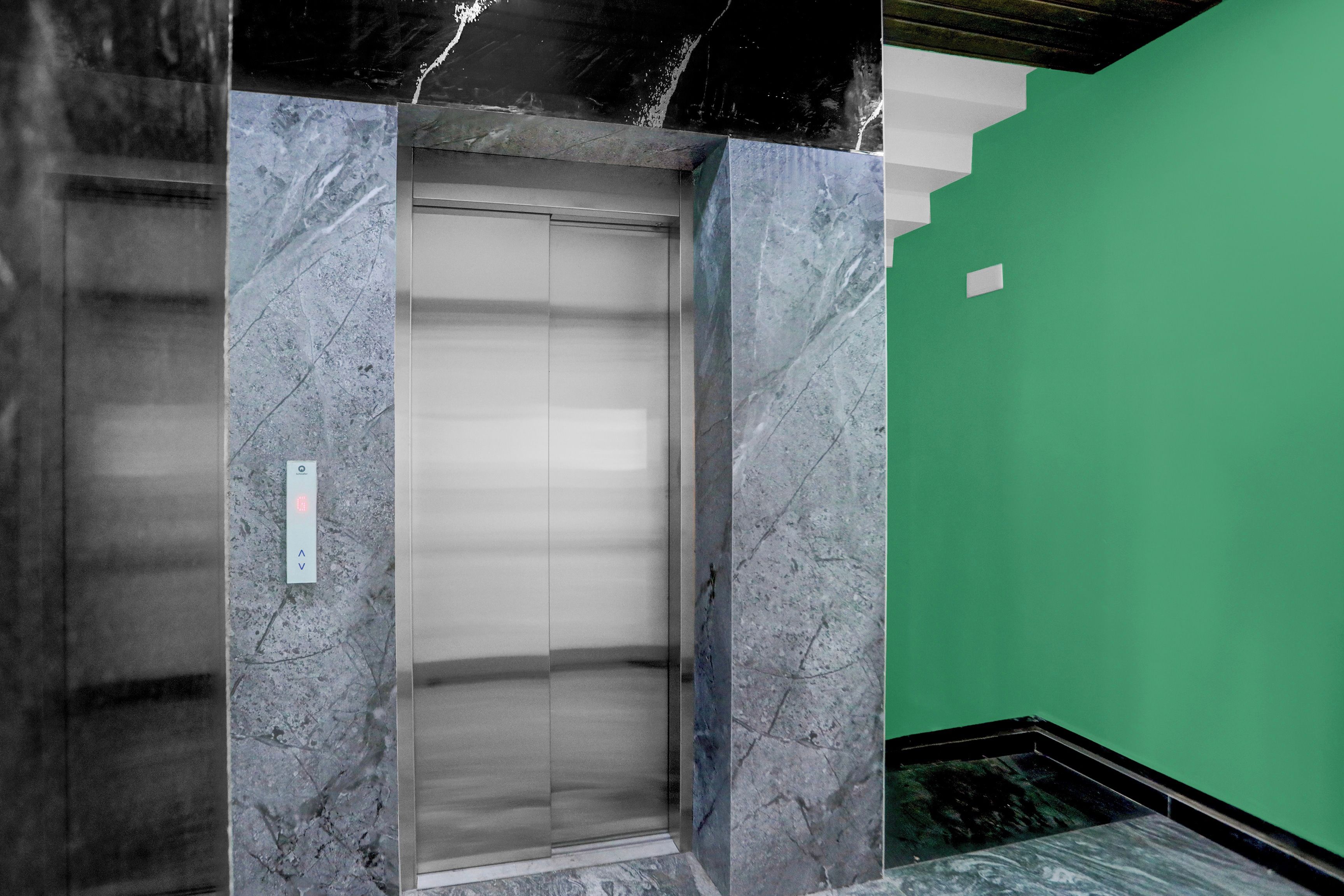 Un ascensor con paredes de mármol y una pared verde aledaña.