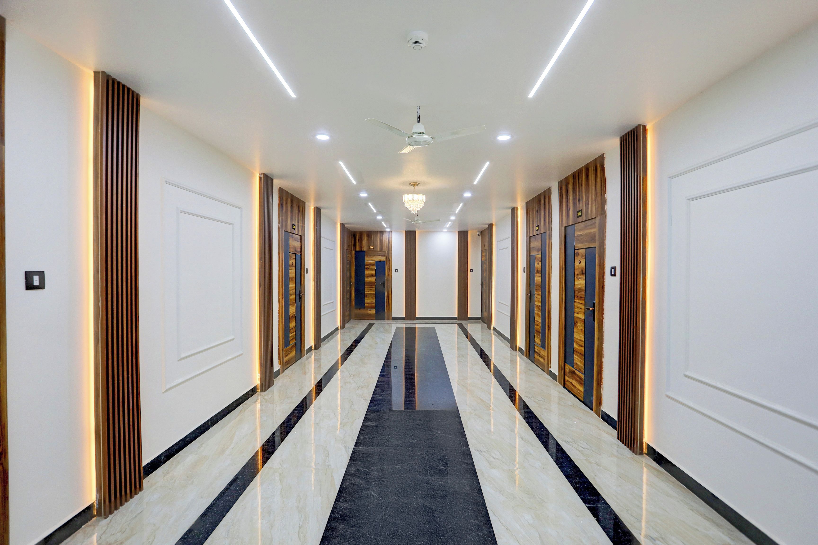 Un largo pasillo bien iluminado con piso de mármol, paneles de madera en las paredes y puertas que dan a diferentes habitaciones.