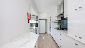 A modern kitchen with white cabinetry, a built-in oven, and a stainless steel range hood. - Shoreline Apartments - unit 13 (Bargara)