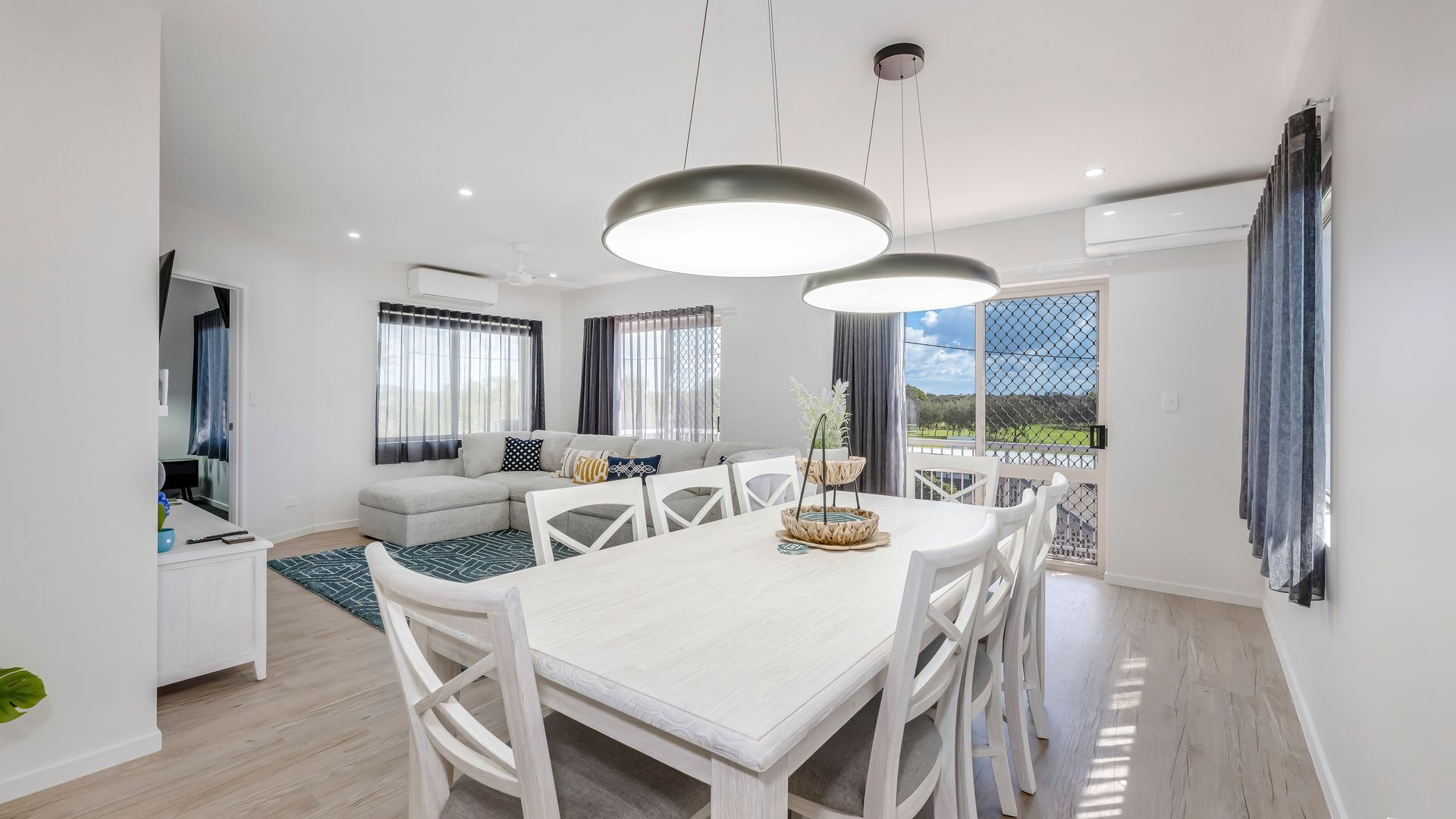 A modern living room with a dining area, large windows, and a view of the outdoors.