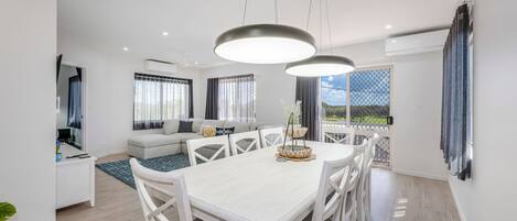 A modern living room with a dining area, large windows, and a view of the outdoors.