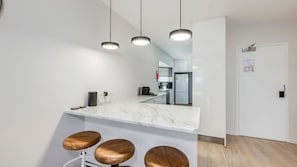 A modern kitchen with a marble countertop, three wooden stools, and pendant lighting. - Shoreline Apartments - unit 13 (Bargara)