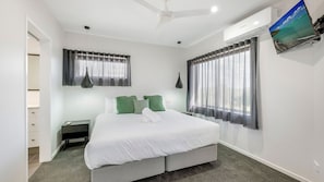 A bedroom with a bed, nightstands, a ceiling fan, and a window with curtains. - Shoreline Apartments - unit 13 (Bargara)