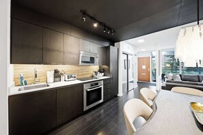 Une cuisine moderne avec des meubles de couleur sombre, des appareils en acier inoxydable et un coin repas comprenant une table et des chaises.