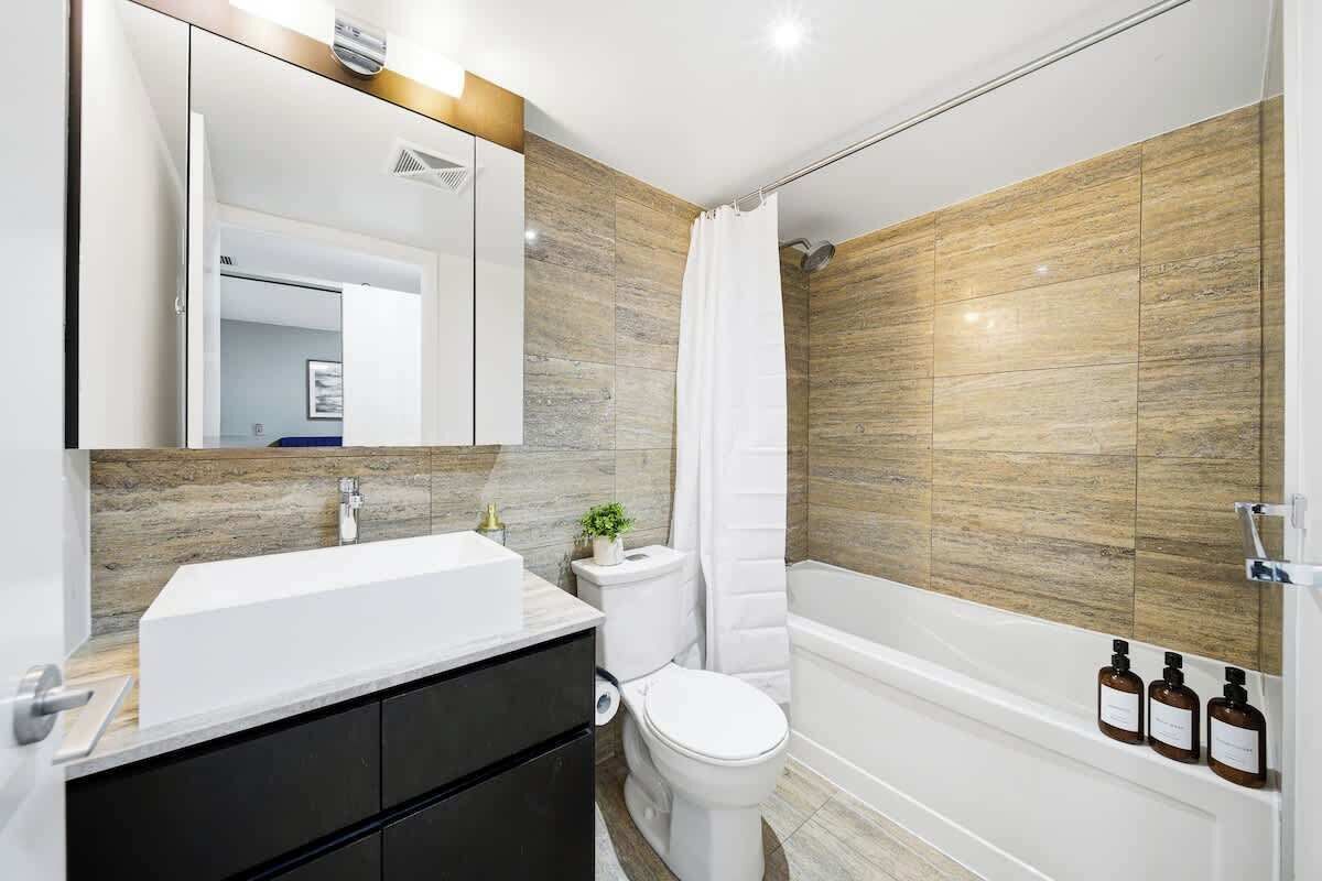 A modern bathroom with a white sink, dark cabinets, a toilet, and a bathtub.