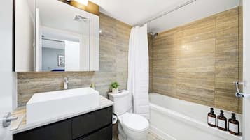 A modern bathroom with a white sink, dark cabinets, a toilet, and a bathtub.
