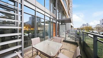 A modern outdoor seating area with a glass railing, a table, and chairs.
