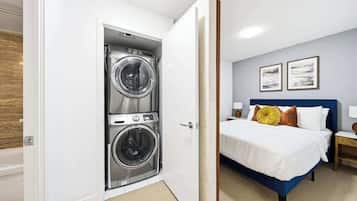 A hotel room with a bed, a nightstand, a lamp, a wall-mounted artwork, and a door leading to a laundry area with two washing machines.