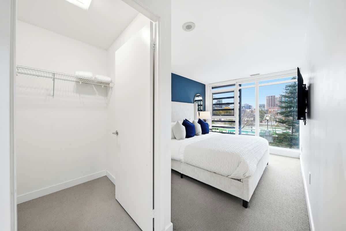 A bedroom with a large bed, a window with a city view, and a door leading to a closet.