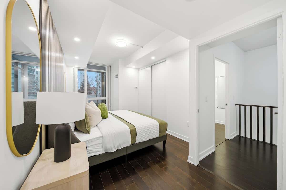 A modern bedroom with a bed, bedside table, and a large mirror.