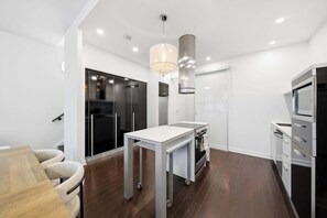 A modern kitchen with a white table, stainless steel appliances, and a chandelier.