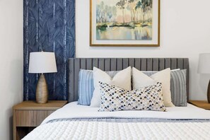 A neatly made bed with a patterned pillow, a bedside lamp, and a framed painting on the wall.