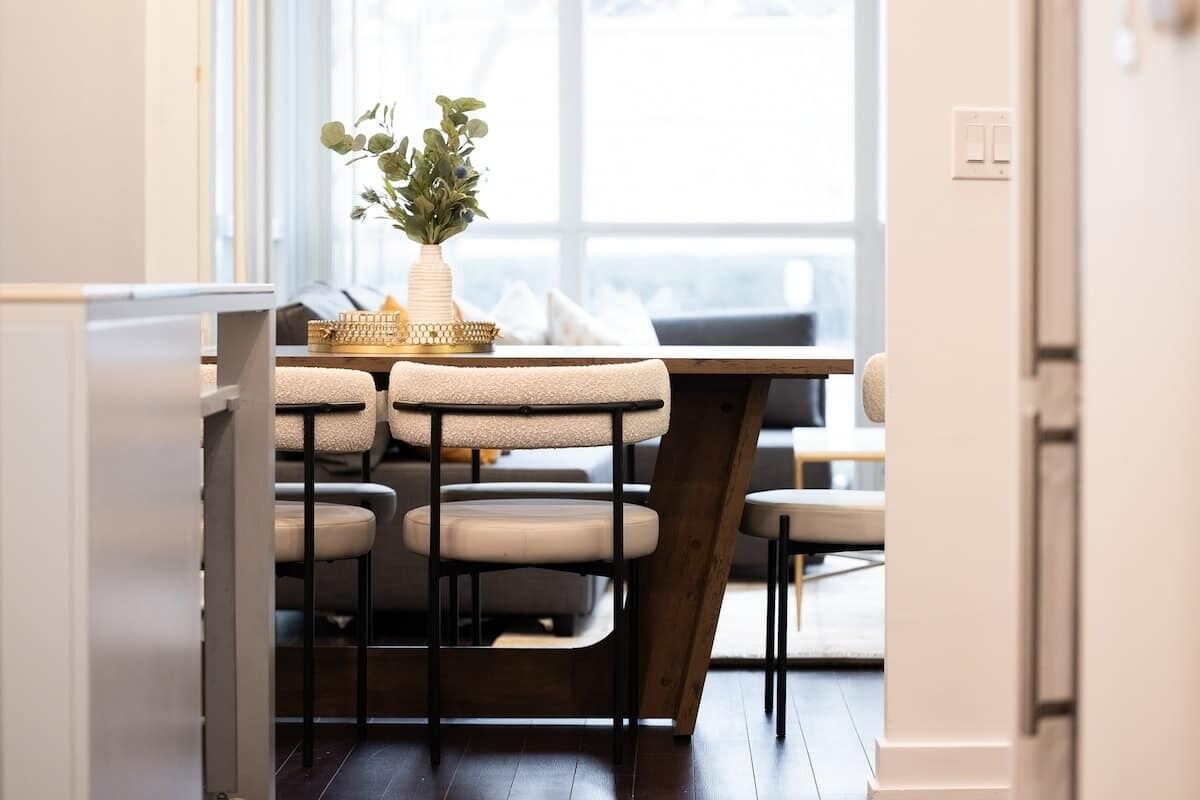 A dining area with a wooden table and chairs, a vase with greenery, and a basket on the table.