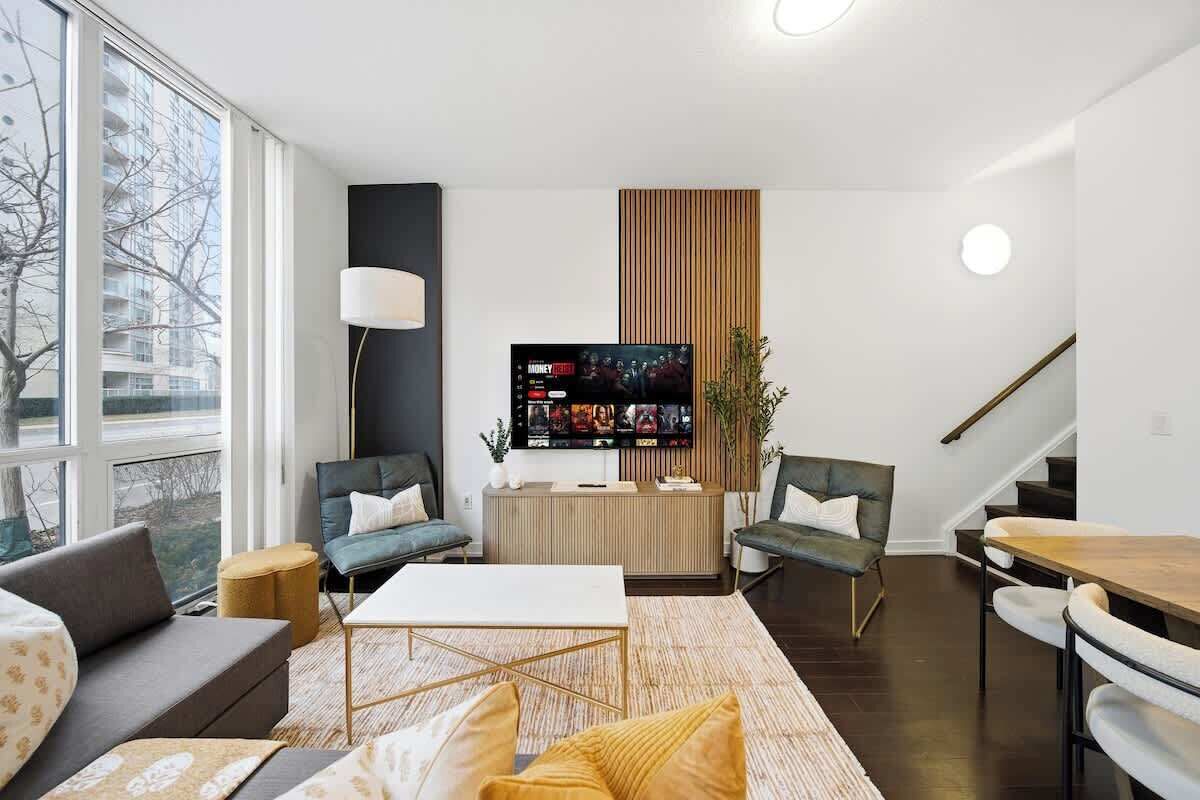 A modern living room with a flat-screen TV, a sofa, a coffee table, and a dining area with chairs.