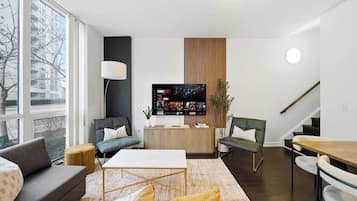 A modern living room with a flat-screen TV, a sofa, a coffee table, and a dining area with chairs.