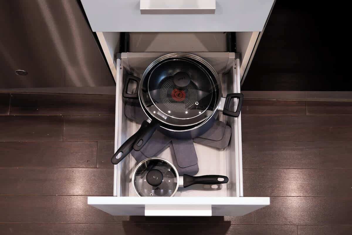A drawer with cookware including a frying pan, a saucepan, and a pot.