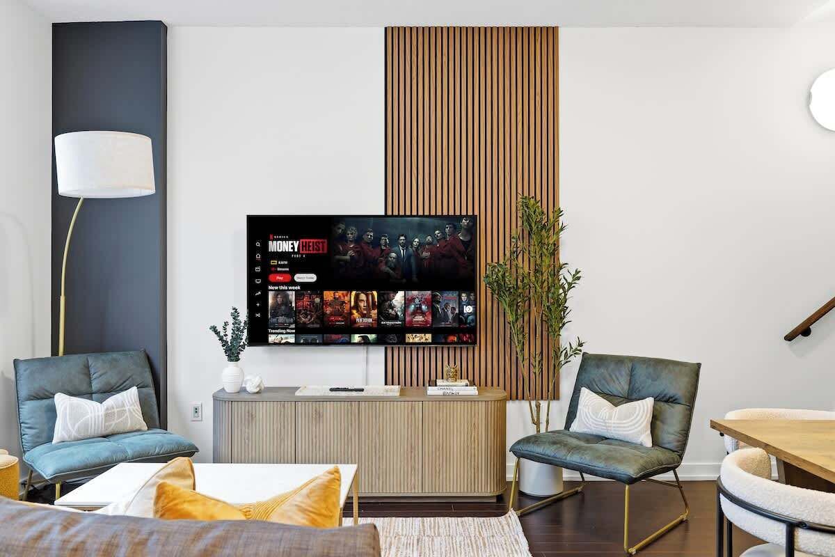 A modern living room with a flat-screen TV mounted on the wall, a wooden cabinet, and two leather armchairs.