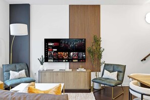 A modern living room with a flat-screen TV mounted on the wall, a wooden cabinet, and two leather armchairs.