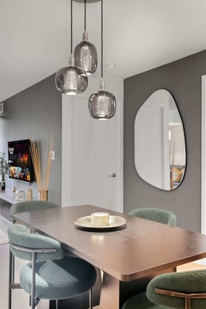 Un espace de salle à manger moderne, avec une longue table, des chaises à revêtement vert et des luminaires suspendus.