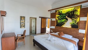 A hotel room with a bed, a desk, a chair, a door, and a large painting on the wall. - Pondok Bali 2 Homestay (Canggu)