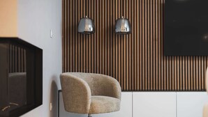 A modern living room with a curved armchair, a flat-screen TV, and two wall-mounted lamps against a wooden panel wall. - Designer Flagship for 6 - by Presidential Palace (Bratislava)