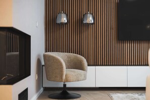 A modern living room with a curved armchair, a flat-screen TV, and two wall-mounted lamps against a wooden panel wall. - Designer Flagship for 6 - by Presidential Palace (Bratislava)