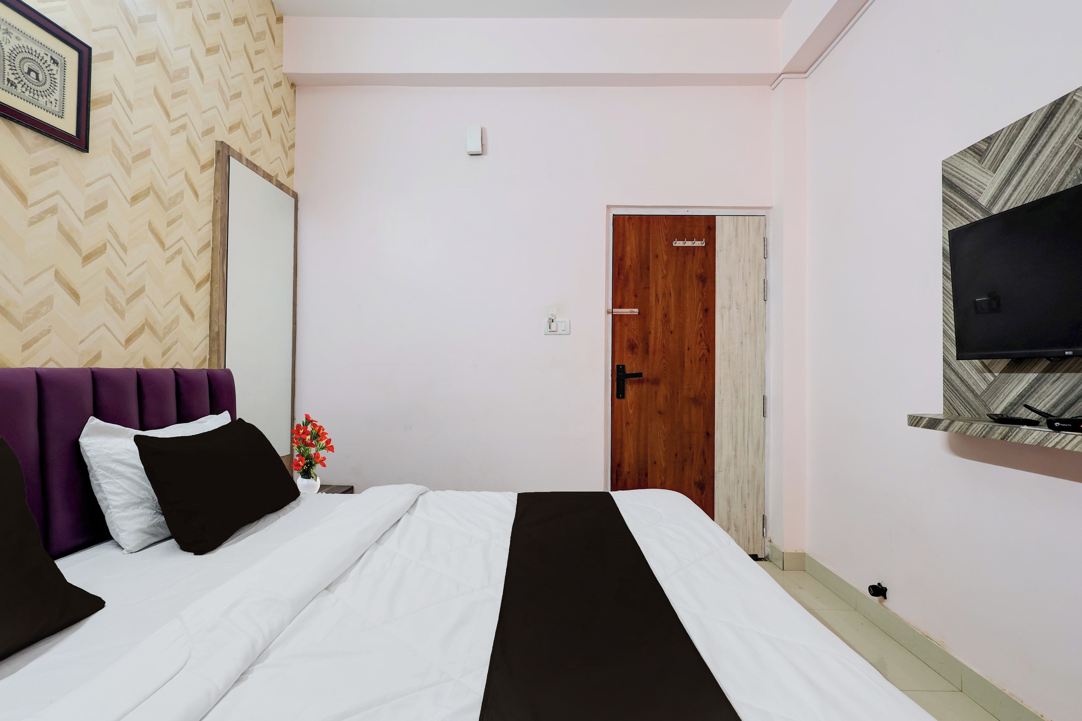 A bedroom with a bed, a television mounted on the wall, and a door leading to another room.