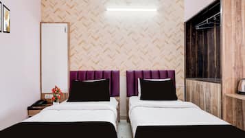 Habitación de hotel con dos camas, un espejo, un armario de madera y una mesita con un florero.