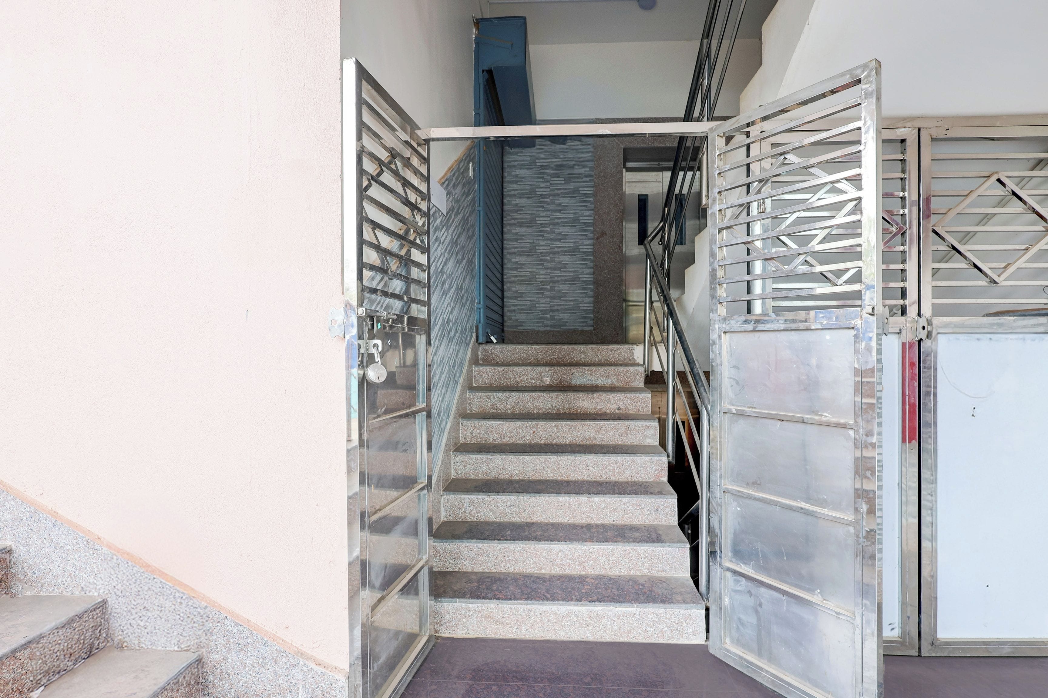 Una escalera que lleva a un rellano con una reja metálica y una puerta de cristal.