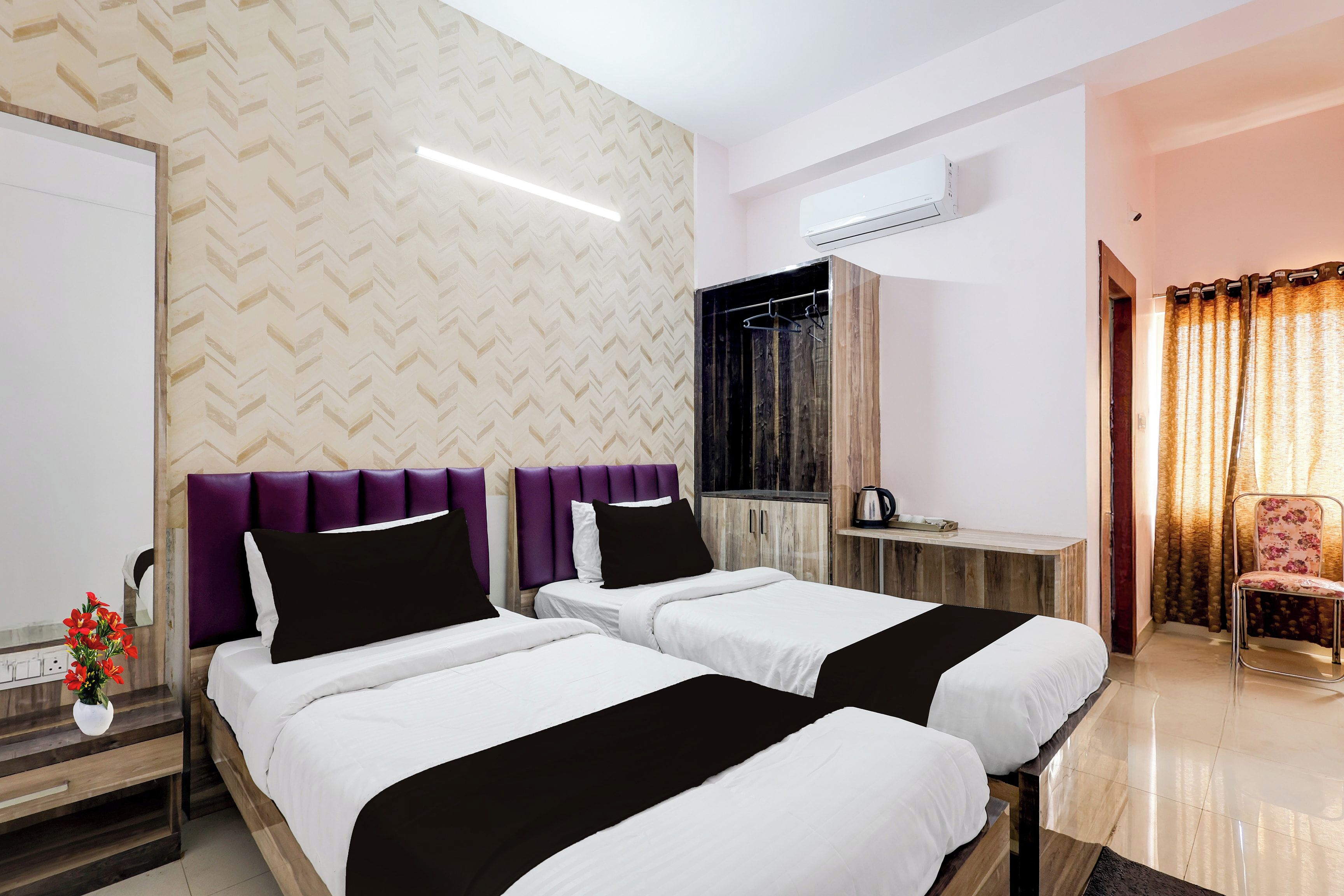 Una habitación de hotel con dos camas, un tocador con espejo, un armario, un equipo de aire acondicionado y una ventana con cortinas.
