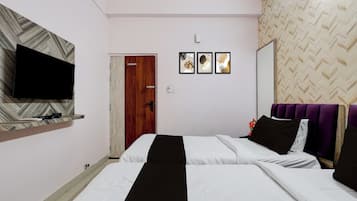 A hotel room with a bed, a television on a shelf, a door, and three framed pictures on the wall.