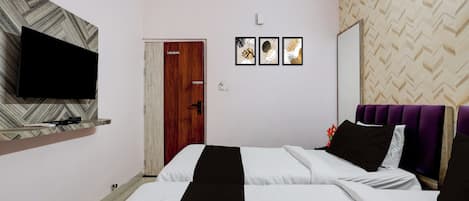A hotel room with a bed, a television on a shelf, a door, and three framed pictures on the wall.