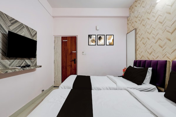 A hotel room with a bed, a television on a shelf, a door, and three framed pictures on the wall.