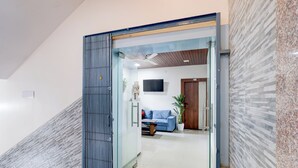 A modern interior with a glass door leading to a living area featuring a sofa, a coffee table, and a television. - Collection O Baramunda Bus Terminal (Bhubaneswar)