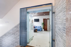 A modern interior with a glass door leading to a living area featuring a sofa, a coffee table, and a television. - Collection O Baramunda Bus Terminal (Bhubaneswar)