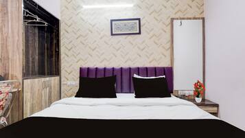 Habitación de hotel con cama, cabecera, un cuadro colgado en la pared, armario y mesita de noche con un jarrón de flores.