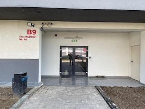 Ein Gebäudeeingang mit einer schwarzen Tür, einem Mülleimer und einem Schild mit der Aufschrift 'B9 Str. MADRID Nr. 46'.