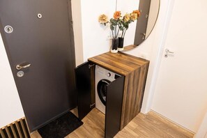 Ein kleines Zimmer mit Waschmaschine, einem kleinen Holztisch und einem Spiegel darüber.