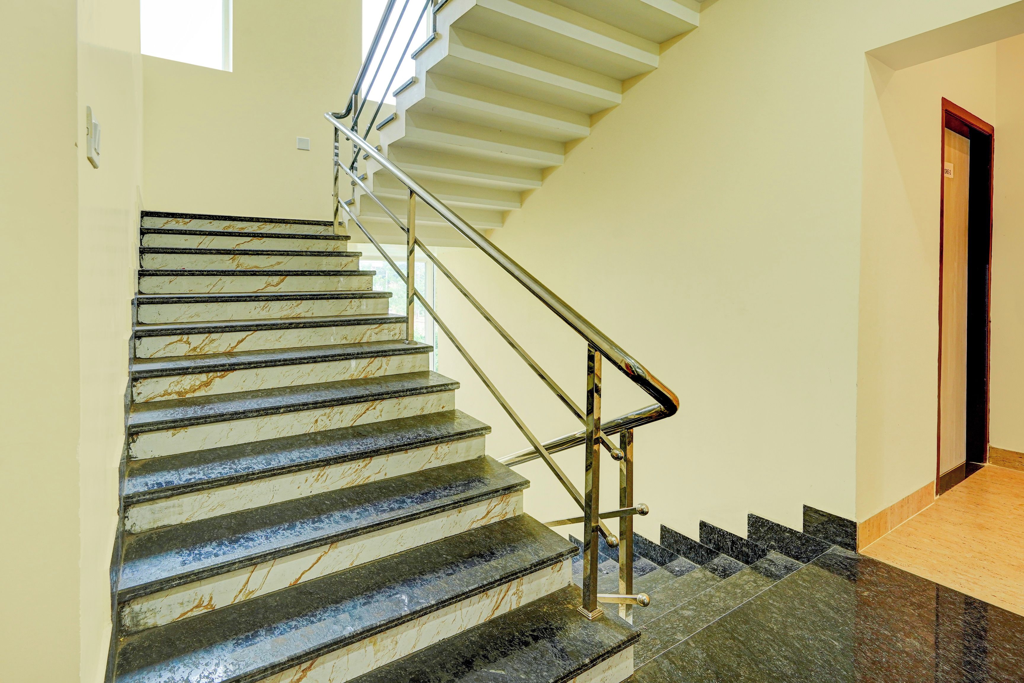 Una escalera con escalones de mármol y barandillas metálicas, que lleva a un rellano con una puerta.