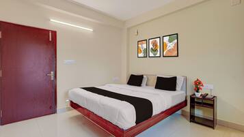 Una habitación de hotel con cama, mesita de noche, toma de corriente y puerta.